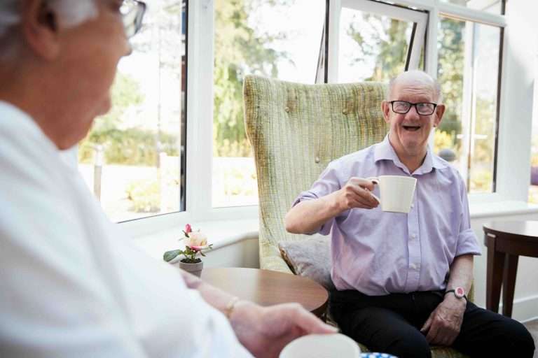 Male And Female Residents Sitting In Chairs and Talking In Retirement Home